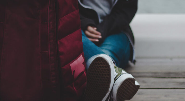 Persons sitting against wall with only shoes and bag visible